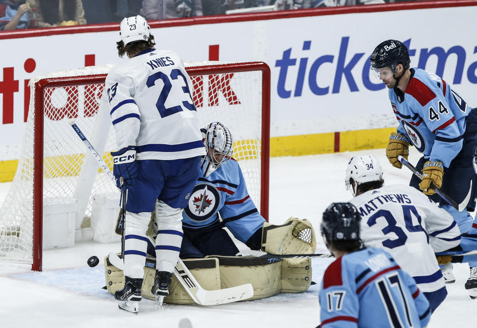 Winnipeg Jets goaltender Connor Hellebuyck (37) saves the shot from Toronto Maple Leafs' Auston Matthews (34) as Matthew Knies (23) tries to screen him during the second period of an NHL hockey game, Saturday, Jan. 27, 2024, in Winnipeg, Manitoba. (John Woods/The Canadian Press via AP)