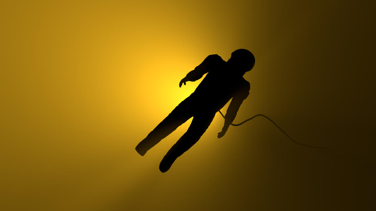  The silhouette of a spacesuit floats with a tether in front of a yellow-lit background, which fades to black toward the right. 