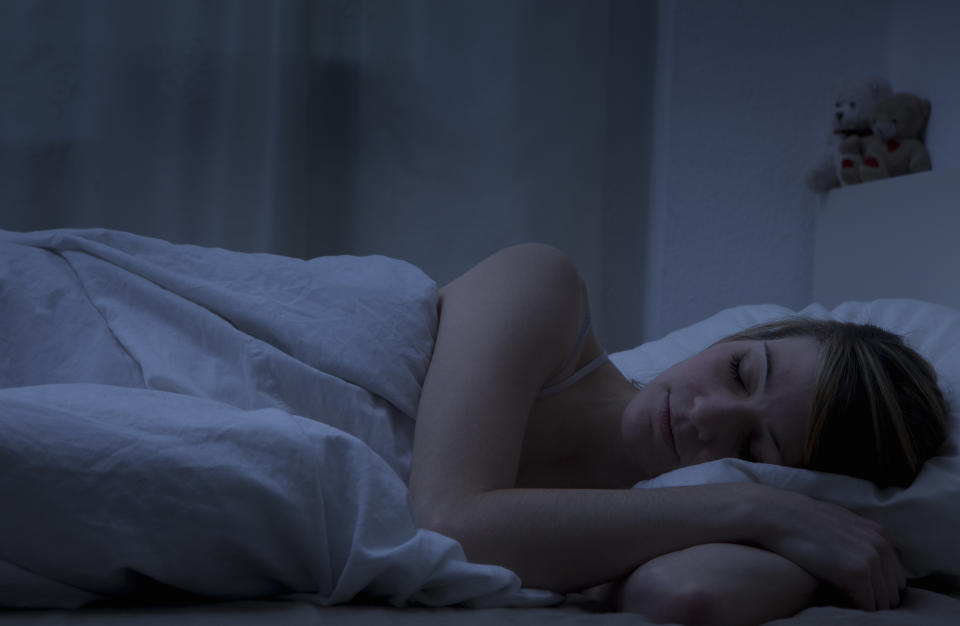 Person sleeping peacefully in a bed with white bedding, a small stuffed bear is visible in the background