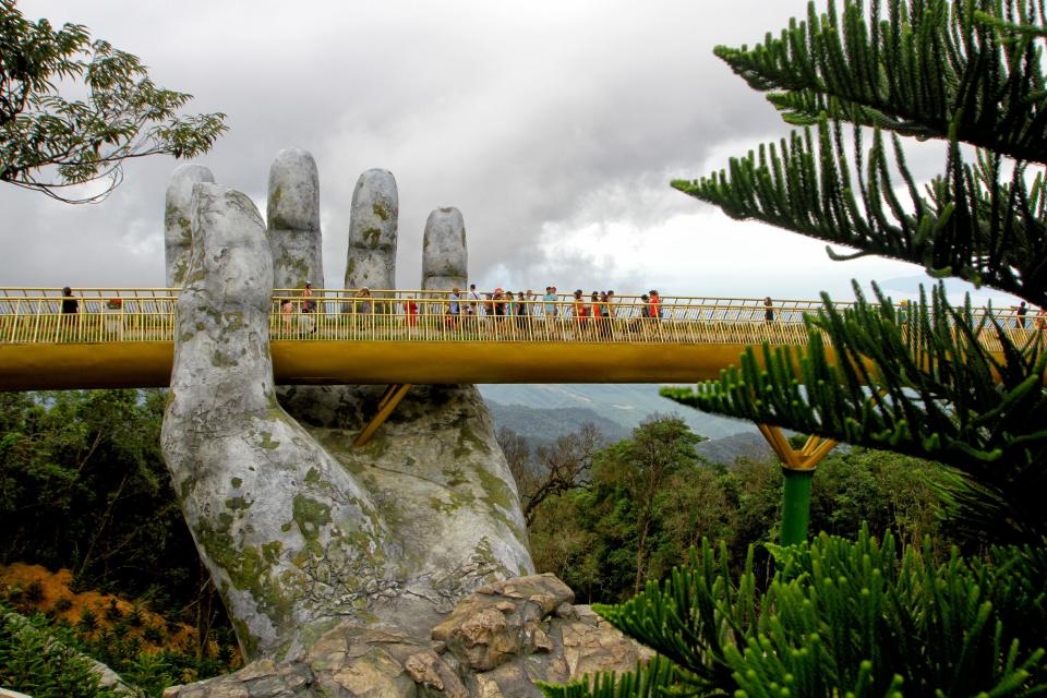 Nestled in the forested hills of central Vietnam, two giant concrete hands emerge from the trees, holding up a glimmering golden bridge crowded with gleeful visitors taking selfies at the country's latest eccentric tourist draw.