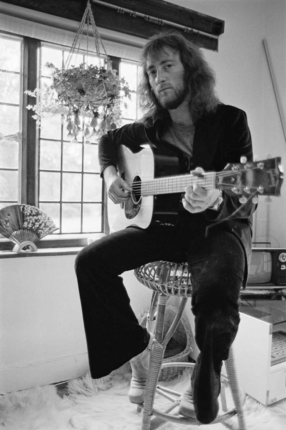 Roger Glover sitting on a stool with an acoustic guitar