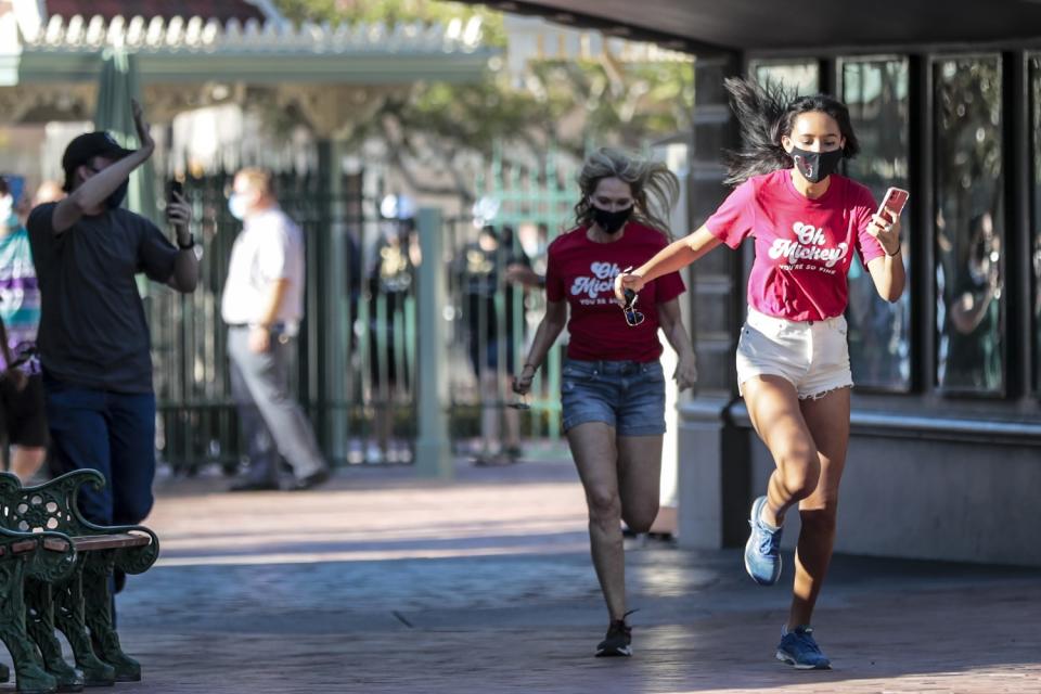 Two girls in masks and "Oh Mickey!" shirts run into Disneyland