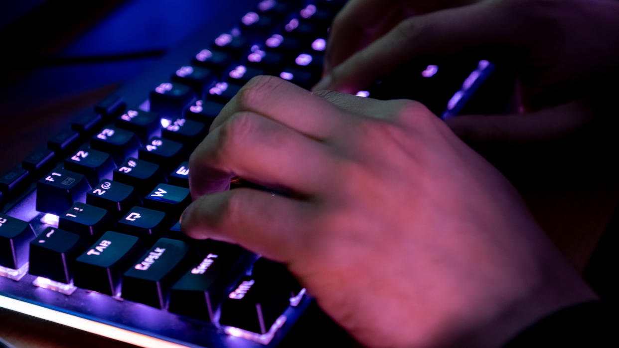  A person typing on a keyboard which has purple backlighting under the keys. 