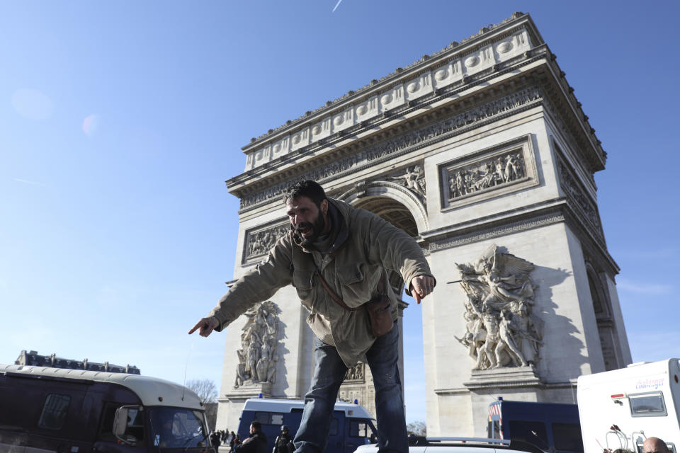 A protester stands atop a vehicle as the convoy drives past the Arc de Triomphe on the Champs-Elysees avenue, Saturday, Feb.12, 2022 in Paris. Paris police intercepted at least 500 vehicles attempting to enter the French capital in defiance of a police order to take part in protests against virus restrictions inspired by the Canada's horn-honking "Freedom Convoy." . (AP Photo/Adrienne Surprenant)