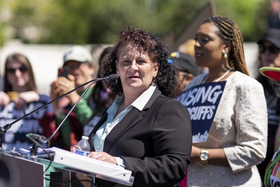 A woman in a suit jacket stands at an outdoor podium