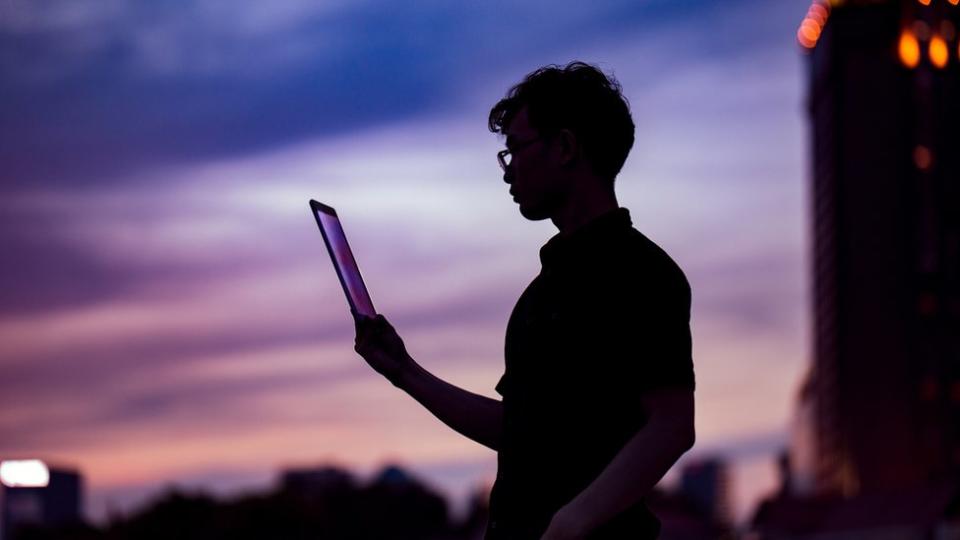 Un joven lee una tableta al atardecer