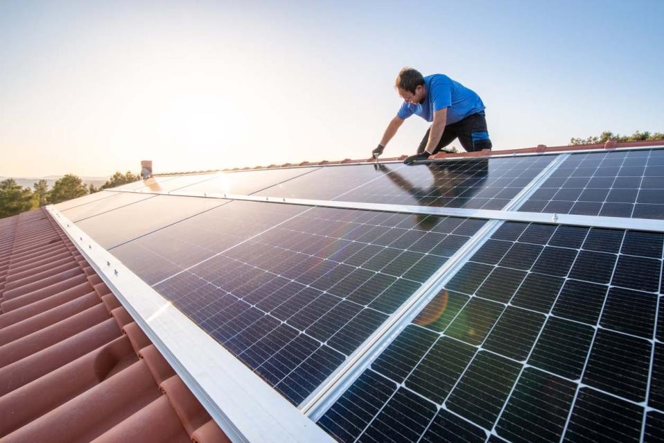 A worker installs solar panels on a roof.