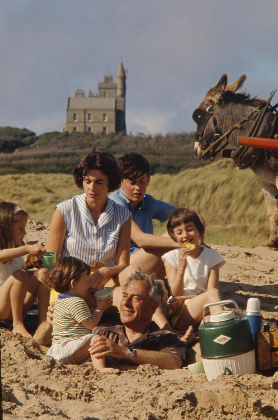 At the beach in front of Classiebawn Castle, Louis Mountbatten, 1st Earl Mountbatten of Burma (1900 - 1979) (center, buried in sand) plays his daughter, Lady Patricia Bradbourne (later 2nd Countess Mountbatten of Burma), and her children, from left, Joanna, Philip, Norton (later Lord Brabourne, in back), and Amanda, County Sligo, Ireland, 1963. (Photo by Ralph Crane/The LIFE Picture Collection via Getty Images)