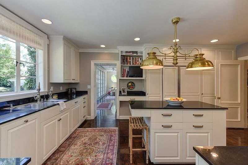 A kitchen in all white with large brass lights above the island