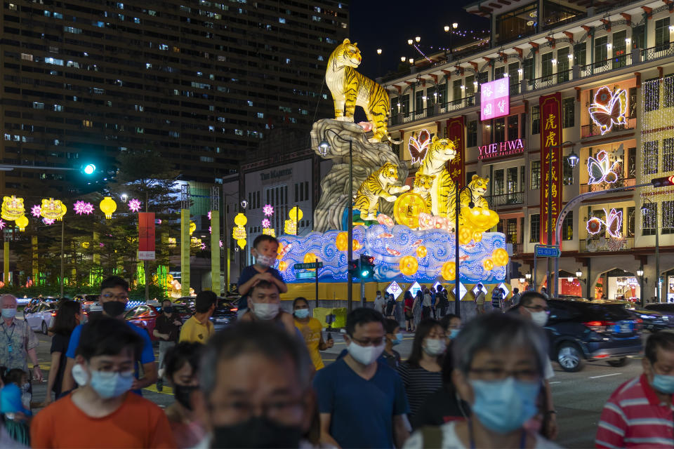 Singapore, Singapore - January 9, 2022: People wearing face masks cross a road before large sculptures of tigers on a street in Chinatown, put up as part of Chinese New Year celebrations. 2022 marks the start of the Year of the Tiger.