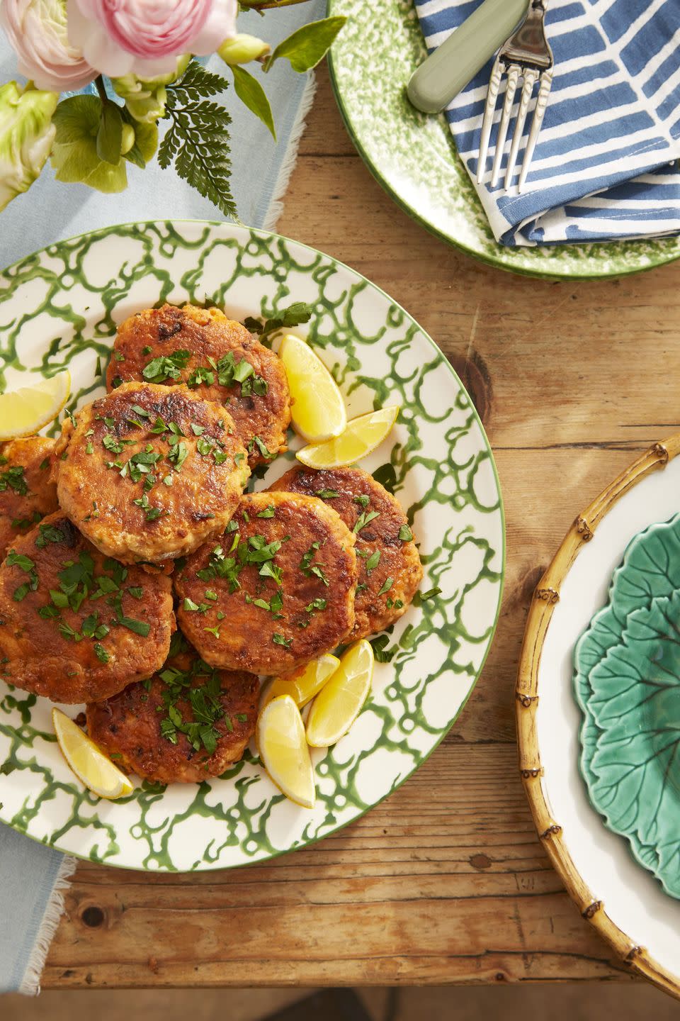 salmon patties arranged on a serving plate with lemon wedges and sprinkled with chopped fresh herbs