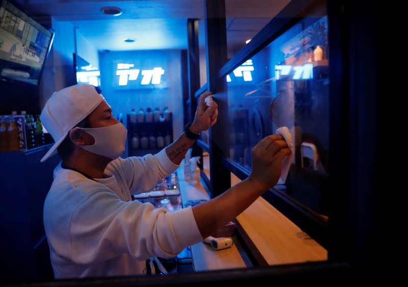 Kazuki Harada, owner of the gay bar New AO, disinfects a plastic panel which was installed to prevent infection, amid the COVID-19 outbreak, at Shinjuku Ni-chome gay district in Tokyo