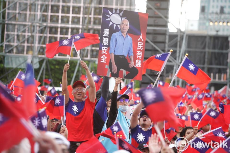 韓粉手拿自製的看板揮舞吶喊，上面印有韓國瑜的照片及其口號「人民有錢、台灣安全」。   圖：張良一 / 攝