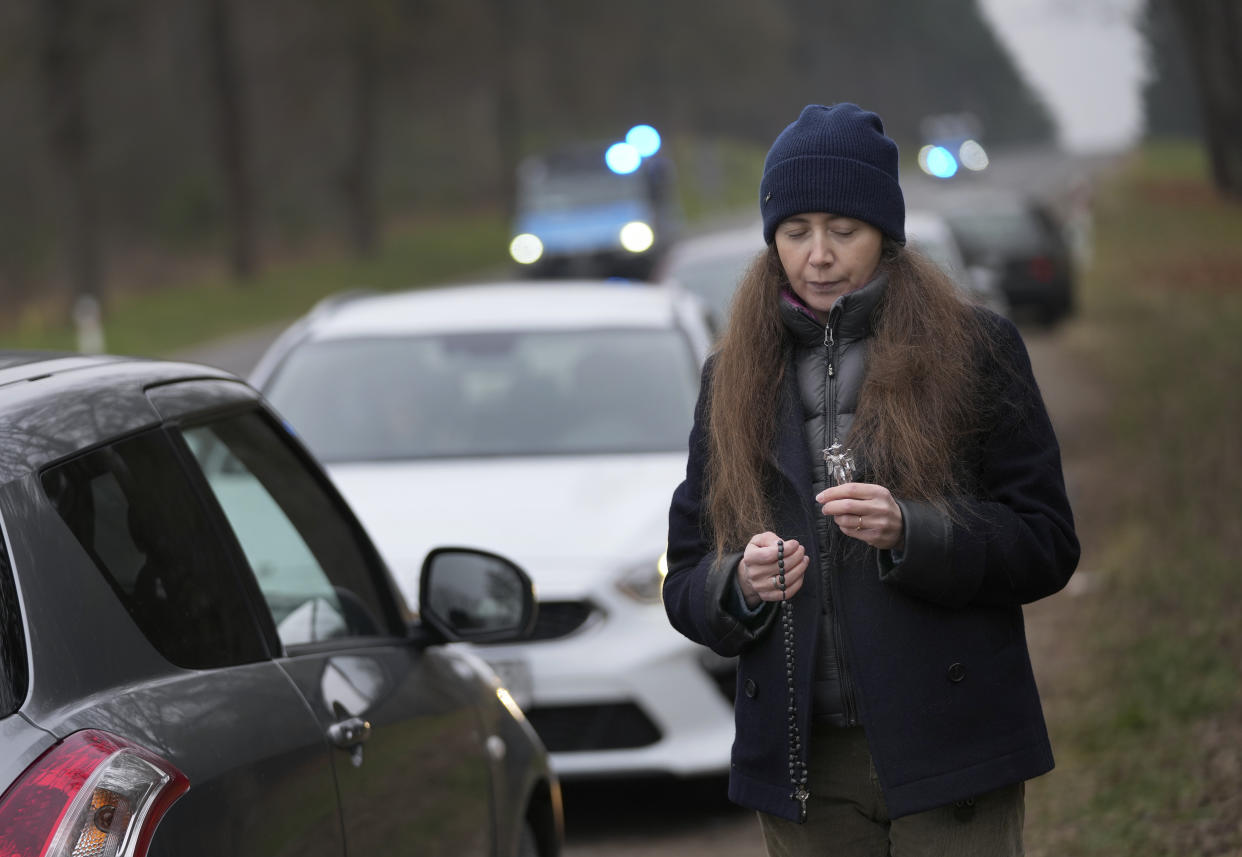 An unidentified woman prays next to a road as police vehicles drive past a check point close to the border with Belarus in Kuznica, Poland, Tuesday, Nov. 16, 2021. (AP Photo/Matthias Schrader)