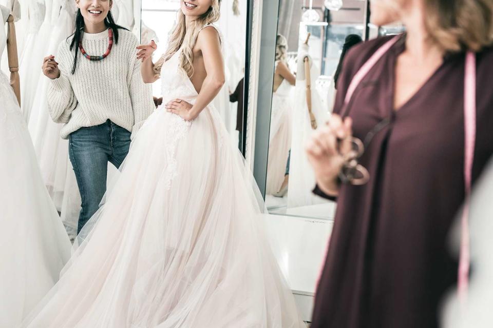 <p>yacobchuk/Getty</p> women looking at wedding dresses