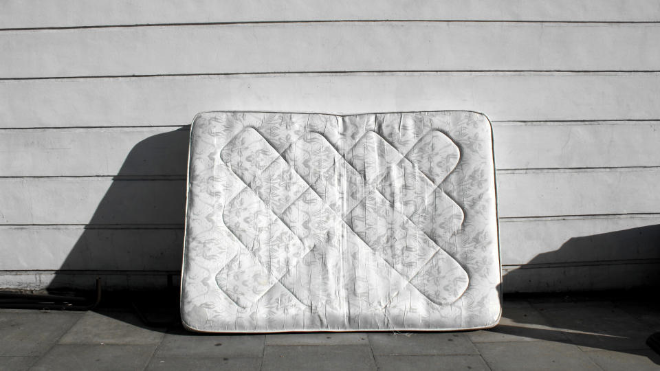 A mattress leans against the side of a building in bright sunlight to dry off after being deep cleaned with a Rug Doctor