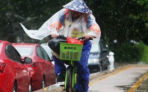 A Chinese sanitation worker rides a bicycle against the strong wind caused by Typhoon Hato on a road along the seacoast in Zhuhai in China's southern Guangdong province - Credit: AFP
