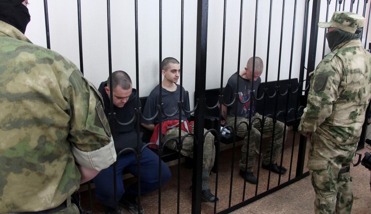 Two British citizens Aiden Aslin, left, and Shaun Pinner, right, and Moroccan Saaudun Brahim, center, sit behind bars in a courtroom in Donetsk, in the territory which is under the Government of the Donetsk People's Republic control, eastern Ukraine, Thursday, June 9, 2022. The two British citizens and a Moroccan have been sentenced to death by pro-Moscow rebels in eastern Ukraine for fighting on Ukraine's side. The three men fought alongside Ukrainian troops and surrendered to Russian forces weeks ago. 