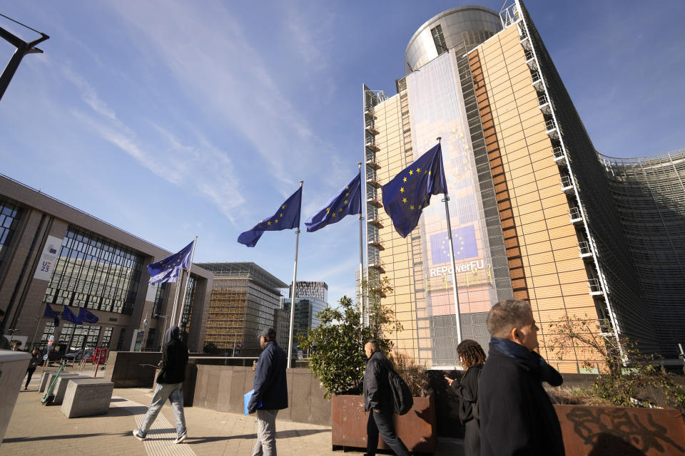 European Union flags flutter in the wind as people walk past EU headquarters, after a shooting on Monday in the center of Brussels, Tuesday, Oct. 17, 2023. Police in Belgium have shot dead a suspected Tunisian extremist accused of killing two Swedish soccer fans in a brazen attack on a Brussels street. European Union institutions are currently remaining closed after a terror alert for Brussels was raised overnight to 4, the top of Belgian's scale, indicating an extremely serious threat. (AP Photo/Virginia Mayo)