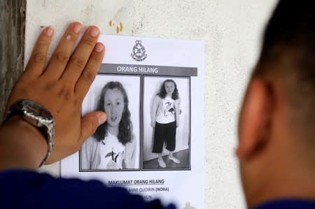 A police officer paste a photo of 15-year-old Irish girl Nora Anne Quoirin who went missing from a resort on a wall at a shop in Seremban.