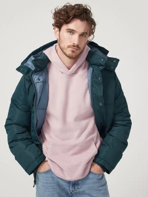 man wearing an open teal blue puffer jacket over a pink hoodie