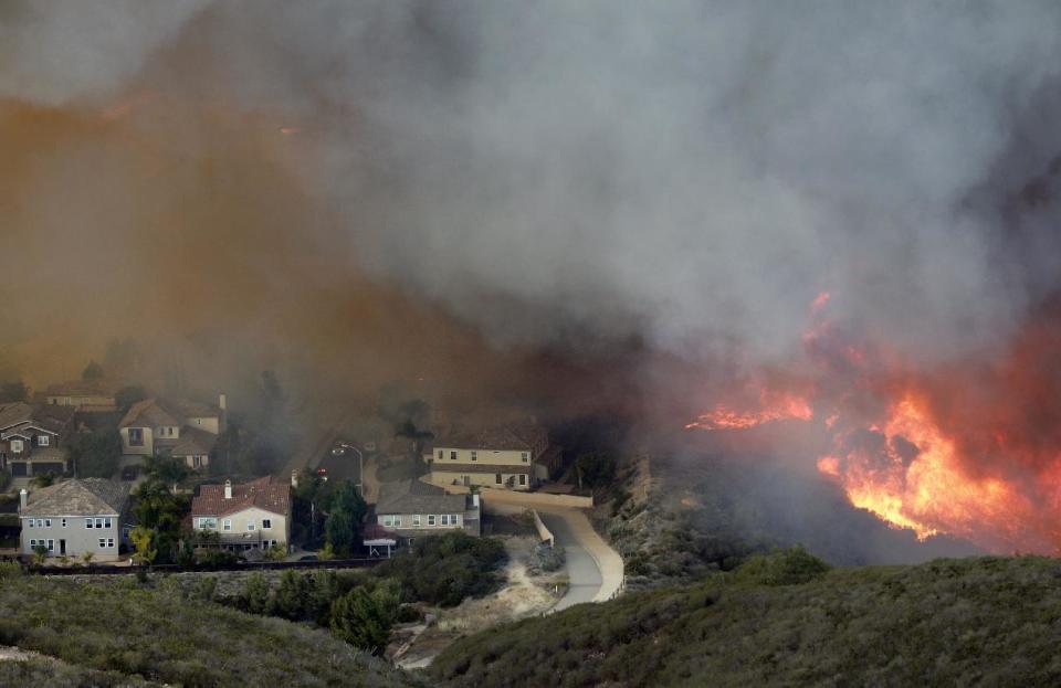 A wildfire approaches homes on Wednesday, May 14, 2014, in San Marcos, Calif. Flames engulfed suburban homes and shot up along canyon ridges in one of the worst of several blazes that broke out Wednesday in Southern California during a second day of a sweltering heat wave, taxing fire crews who fear the scattered fires mark only the beginning of a long wildfire season. (AP Photo/)