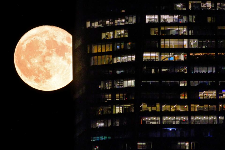 The full moon passes behind the illuminated windows of a New York City skyscraper on Aug. 1, 2023. This is the first of two supermoons in August. A supermoon is broadly defined as a full moon that is closer to the Earth making it appear larger than normal.