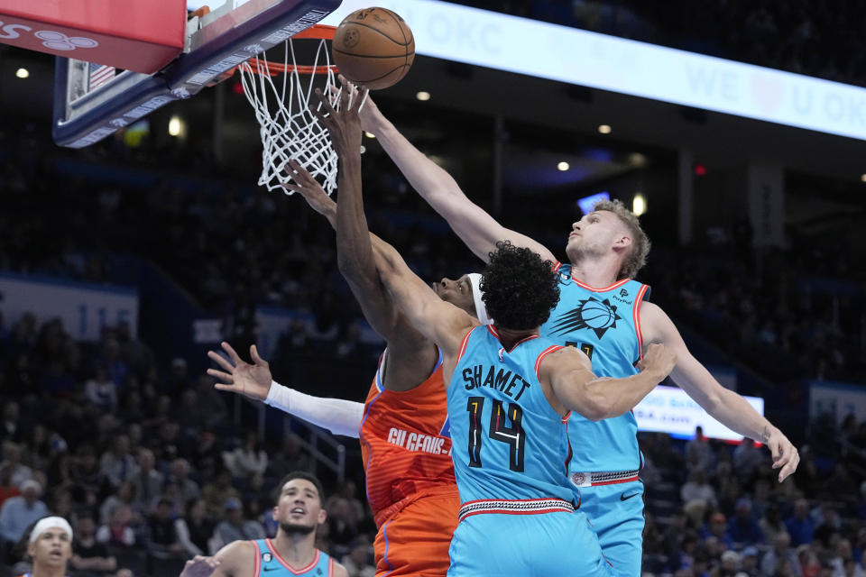 Oklahoma City Thunder guard Shai Gilgeous-Alexander, left, shoots between Phoenix Suns guard Landry Shamet (14) and center Jock Landale, right, in the first half of an NBA basketball game Sunday, March 19, 2023, in Oklahoma City. (AP Photo/Sue Ogrocki)