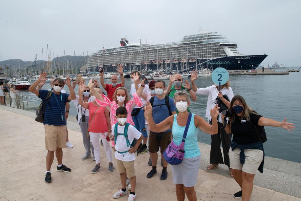 This image shows a group of people standing in front of a cruise ship waving to the camera.