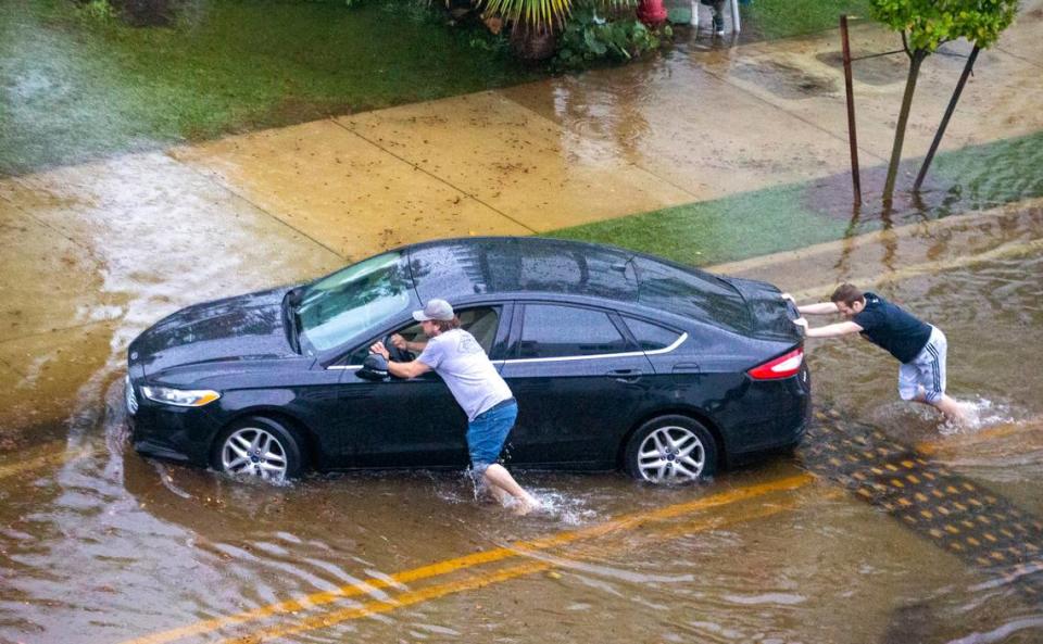 Two men push a stranded car through a flooded road after heavy rains at North Bay Road and 180th Drive in Sunny Isles Beach on Monday, May 25, 2020.