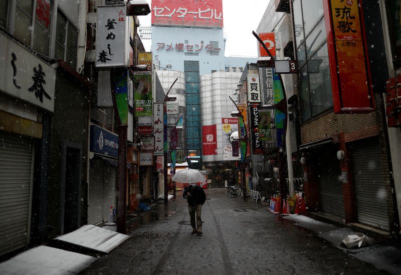 A man wearing a protective face mask, following an outbreak of the coronavirus disease, walks past on an empty street in theasnow fall in Tokyo