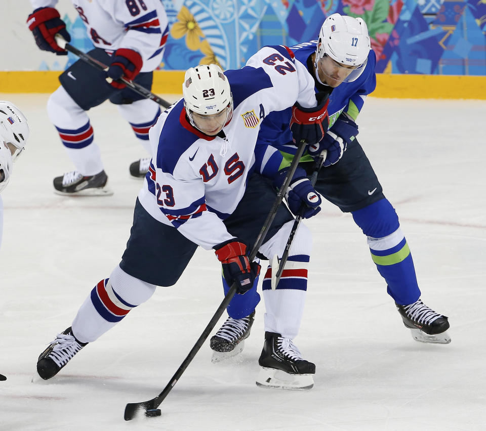 USA forward Dustin Brown takes control of the puck away from Slovenia defenseman Ziga Pavlin during the 2014 Winter Olympics men's ice hockey game at Shayba Arena Sunday, Feb. 16, 2014, in Sochi, Russia. (AP Photo/Petr David Josek)