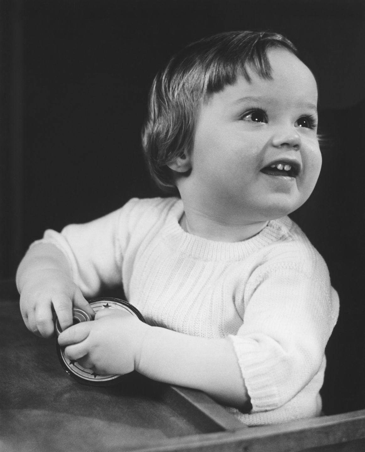 baby girl 9 12 months sitting at table, holding toy bw