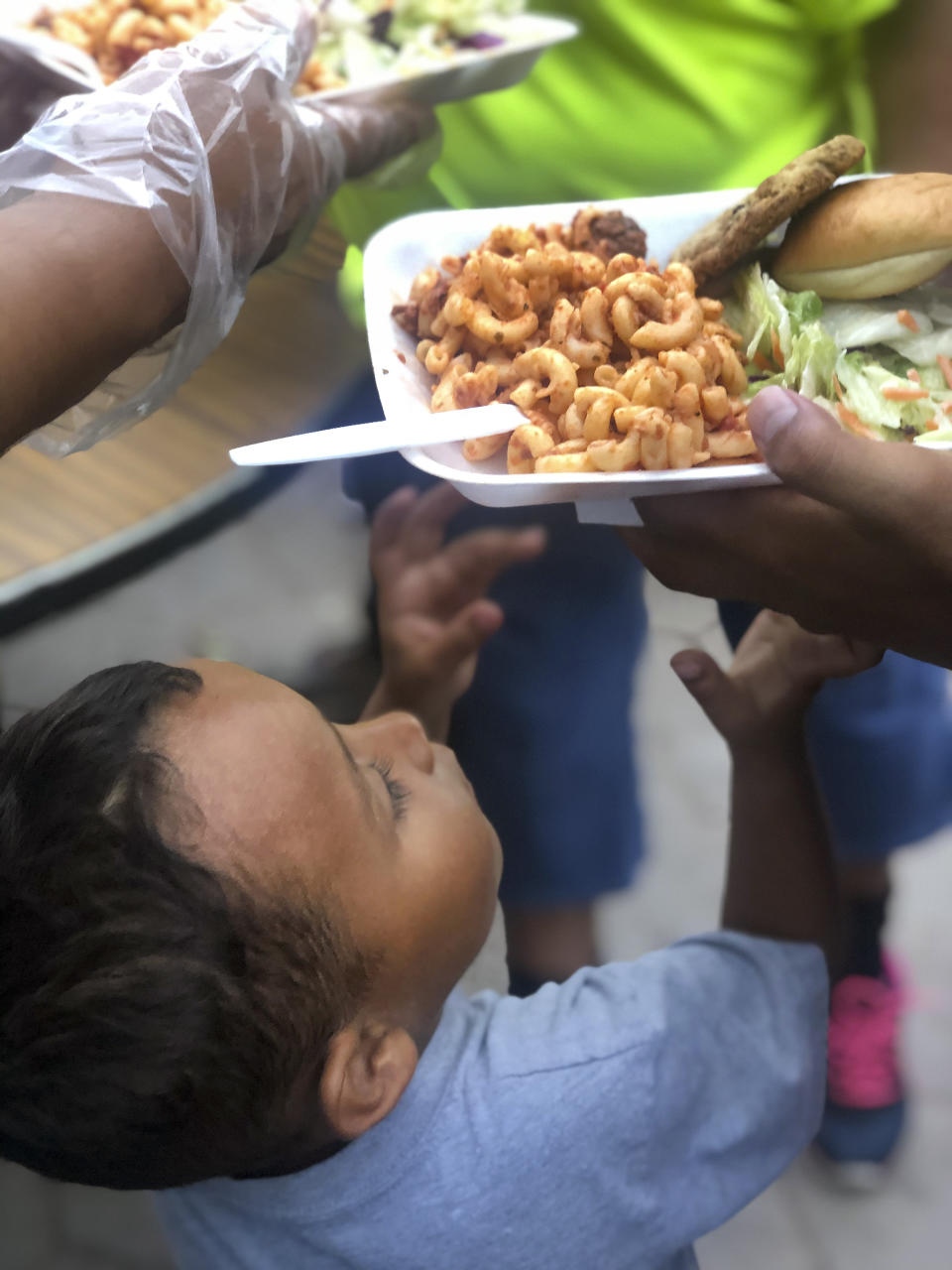 In this October 2019 photo provided by Daniela Dominguez, a child reaches for a meal cooked by a team from the Bay Area Border Relief at a tent encampment in Matamoros, Mexico. Dominguez, assistant professor in counseling psychology at University of San Francisco, said mutual aid networks are part of the Latino culture where people may feel safer getting help from their own community rather than government entities or formal charities. (Daniela Dominguez via AP)