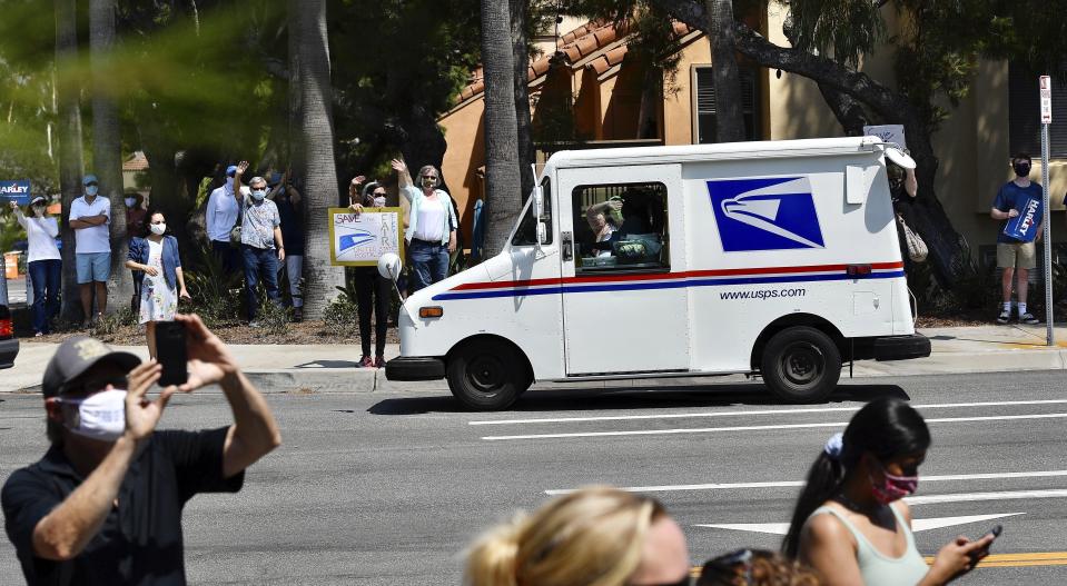 A postal carrier drives past protesters during a rally against changes to the United States Postal Service, in Newport Beach, Calif., Tuesday, Aug., 18, 2020. Facing mounting public pressure and a crush of state lawsuits, President Donald Trump's new postmaster general announced Tuesday he is halting some operational changes to mail delivery that critics blamed for widespread delays and warned could disrupt the November election.(Jeff Gritchen/The Orange County Register via AP)