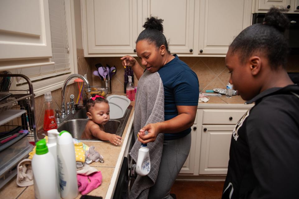 A woman baths an infant in the sink while an older child looks on.