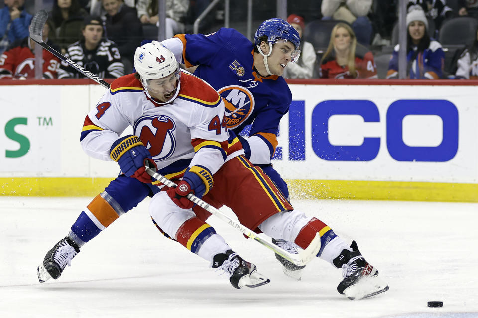 New Jersey Devils left wing Miles Wood (44) is tripped by New York Islanders defenseman Ryan Pulock during the first period of an NHL hockey game Friday, Dec. 9, 2022, in Newark, N.J. (AP Photo/Adam Hunger)