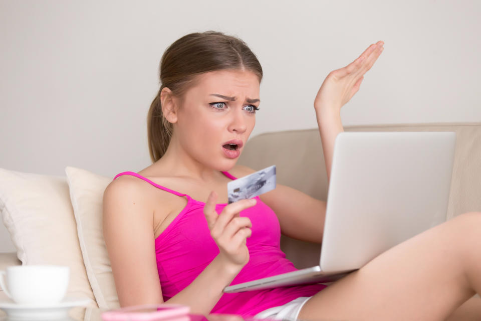 Upset woman with credit card in hand looking on laptop pc screen with confusion while shopping at home. Credit card blocking, internet fraud, empty bank account, online payment mistake, spent too much