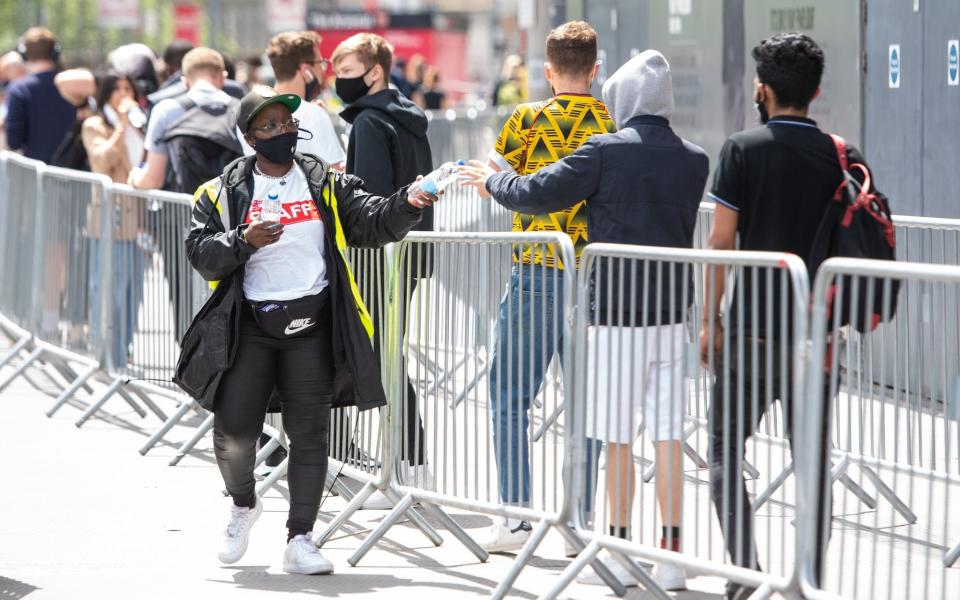 Staff hand out bottles of water as people queue for a mass coronavirus vaccination centre at Arsenal's Emirates Stadium - Dominic Lipinski/PA Wire