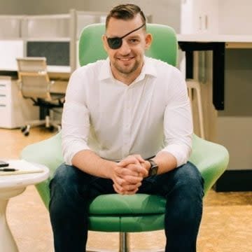 This is a portrait of Erik Goodge who is wearing an eye patch while sitting in a green office chair.
