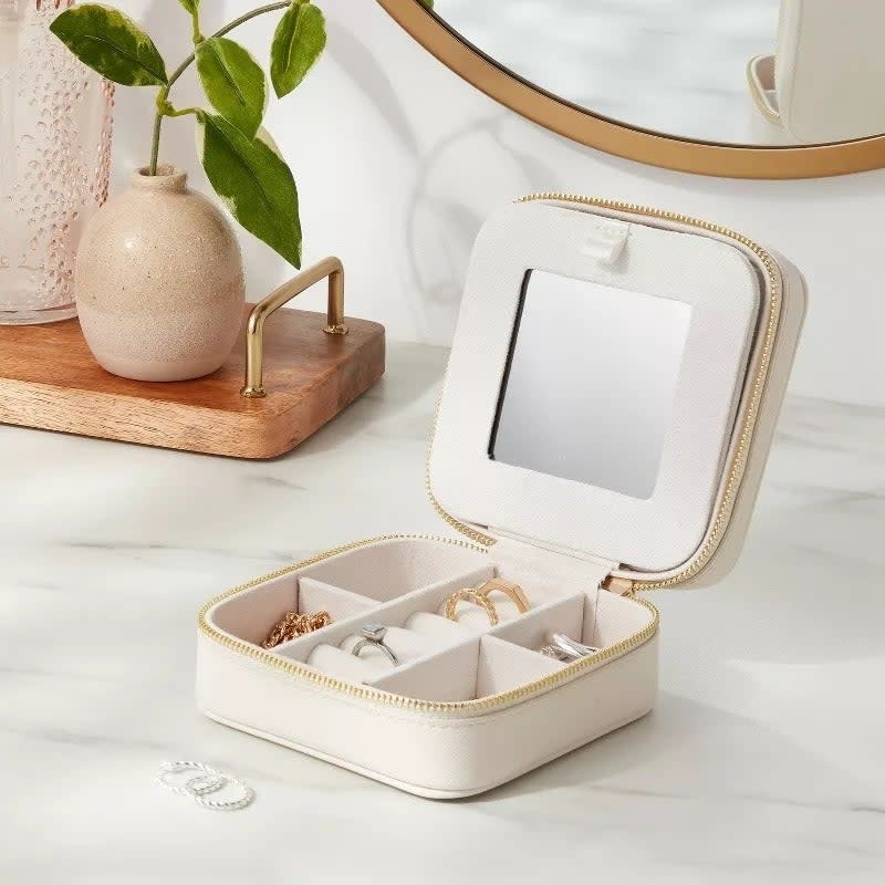 Open jewelry box with mirror and compartments containing various pieces of jewelry on a vanity