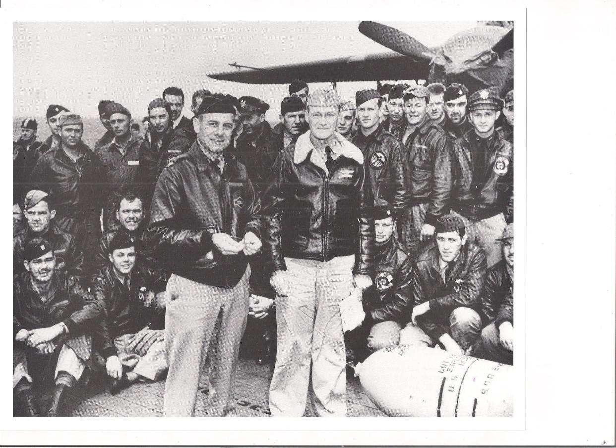 Military servicemen stand aboard the deck of the USS Hornet.