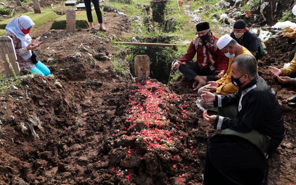 Family members pray during the burial of their relative at a section of Srengseng Sawah Cemetery reserved for those who died of COVID-19, in Jakarta, Indonesia, - Tatan Syuflana /AP