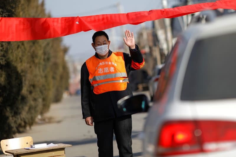 A village committee member wearing face mask and vest, stops a car for checking as he guards at the entrance of a community to prevent outsiders from entering, as the country is hit by an outbreak of the new coronavirus, in Tianjiaying village