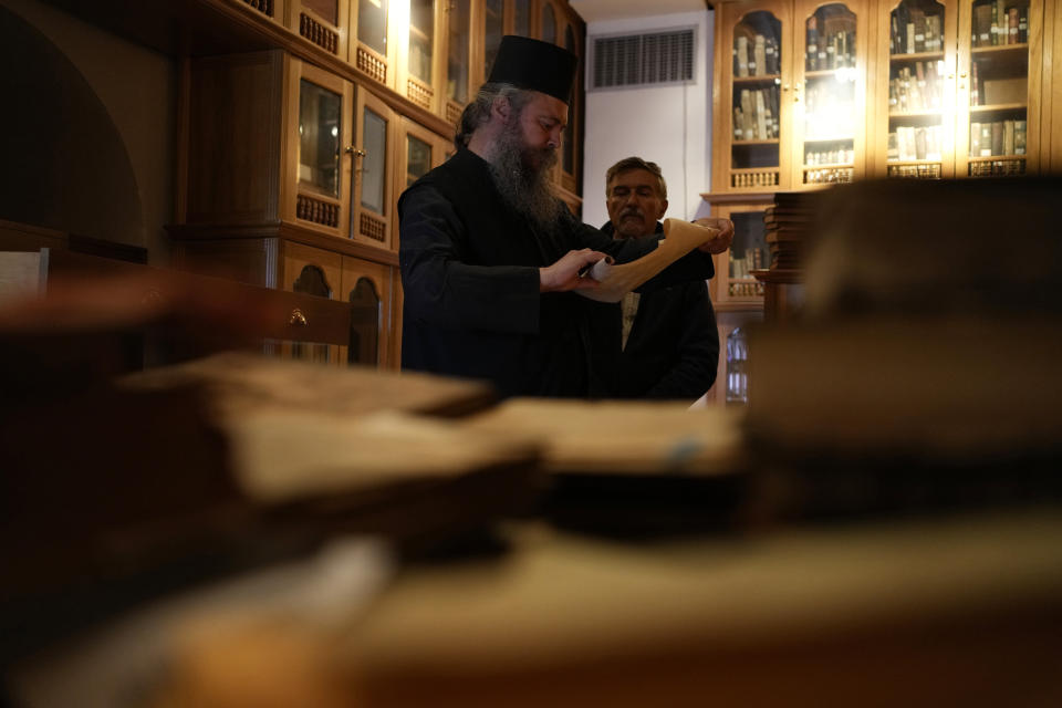 Father Theofilos, a Pantokrator monk reads a manuscript as Anastasios Nikopoulos, a jurist and scientific collaborator of the Free University of Berlin, looks on at the library of Pantokrator Monastery in the Mount Athos, northern Greece, on Thursday, Oct. 13, 2022. Deep inside a medieval fortified monastery in the Mount Athos monastic community, researchers are for the first time tapping a virtually unknown treasure: thousands of Ottoman-era manuscripts that include the oldest of their kind in the world. (AP Photo/Thanassis Stavrakis)