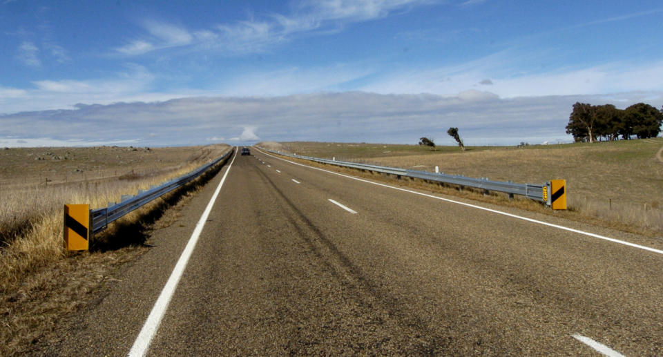 A single car on a wide open two-lane country road. 