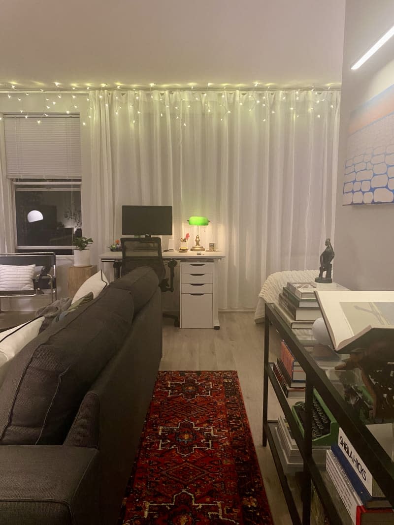 A living room with a grey couch, and red carpet next to an office workspace.