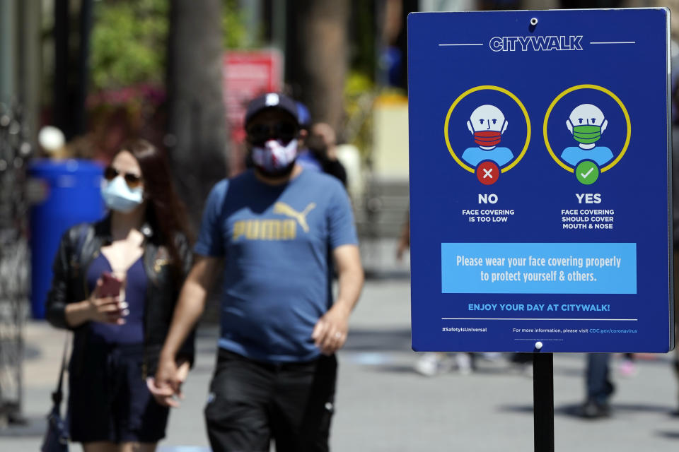 FILE - In this May 14, 2021, file photo, signs instruct visitors on the proper way to wear masks at the Universal City Walk in Universal City, Calif. California is keeping its rules for wearing facemasks in place until the state more broadly lifts its pandemic restrictions on June 15. State officials said Monday, May 17 that the delay will give people time to prepare, and for the state to make sure that virus cases stay low. (AP Photo/Marcio Jose Sanchez, File)