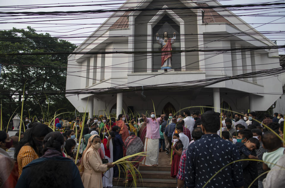 A man, center, wearing mask as a precaution against COVID-19 gestures to devotees to make way for an arriving procession as Christians observe Palm Sunday outside a Church in Kochi, Kerala state, India, Sunday, April 10, 2022. The South Asian country has recorded a steep dip in coronavirus cases in recent weeks, with the health ministry reporting approximately 1,100 cases on Friday. (AP Photo/R S Iyer)