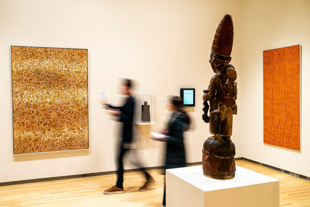 Cory Gundlach, curator of African art at the Stanley Museum of Art, walks with Press-Citizen reporter Paris Barraza towards Golden Enstrata by Richard Pousette-Dart, at left, past an Elefon headdress made of wood from the early 20th century in the foreground and Tingari Cycle by Ronnie Tjampitjinpa at right, Thursday, Jan. 26, 2023, on the University of Iowa campus in Iowa City, Iowa.